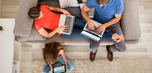 A family of three relaxes on their couch while using multiple internet connected devices.