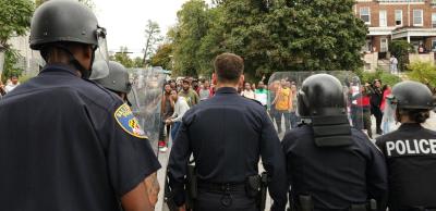 A line of Baltimore Police Officers raises riot shields as it advances on a group of protesters, from HBO's new mini-series "We Own This City"